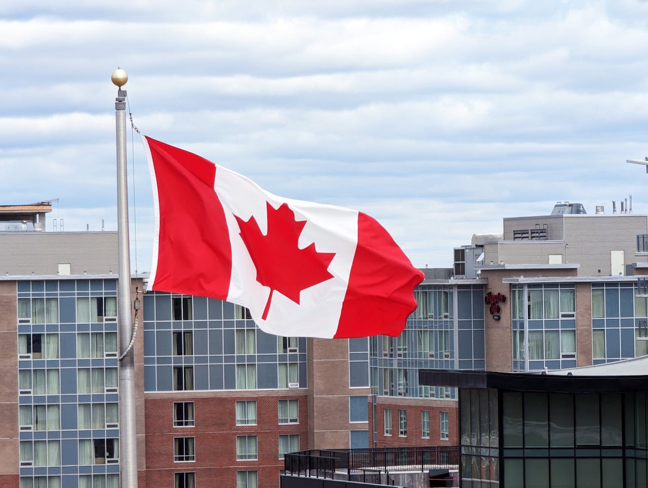 ours-journey Canadian flag on a pole waving against modern buildings in Halifax, Nova Scotia.