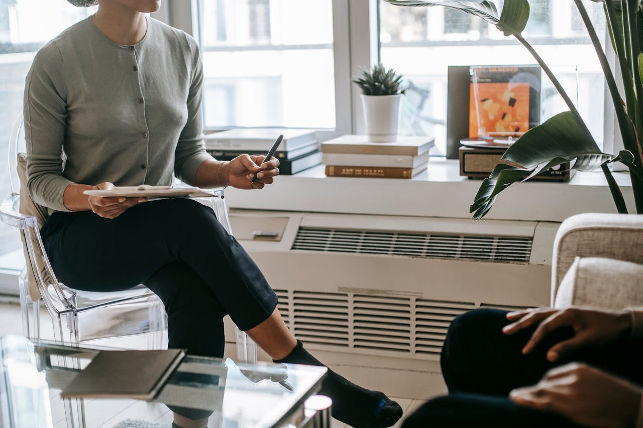 about-02 Unrecognizable female psychologist with crossed legs writing information on clipboard during appointment with anonymous ethnic patient in cozy light office